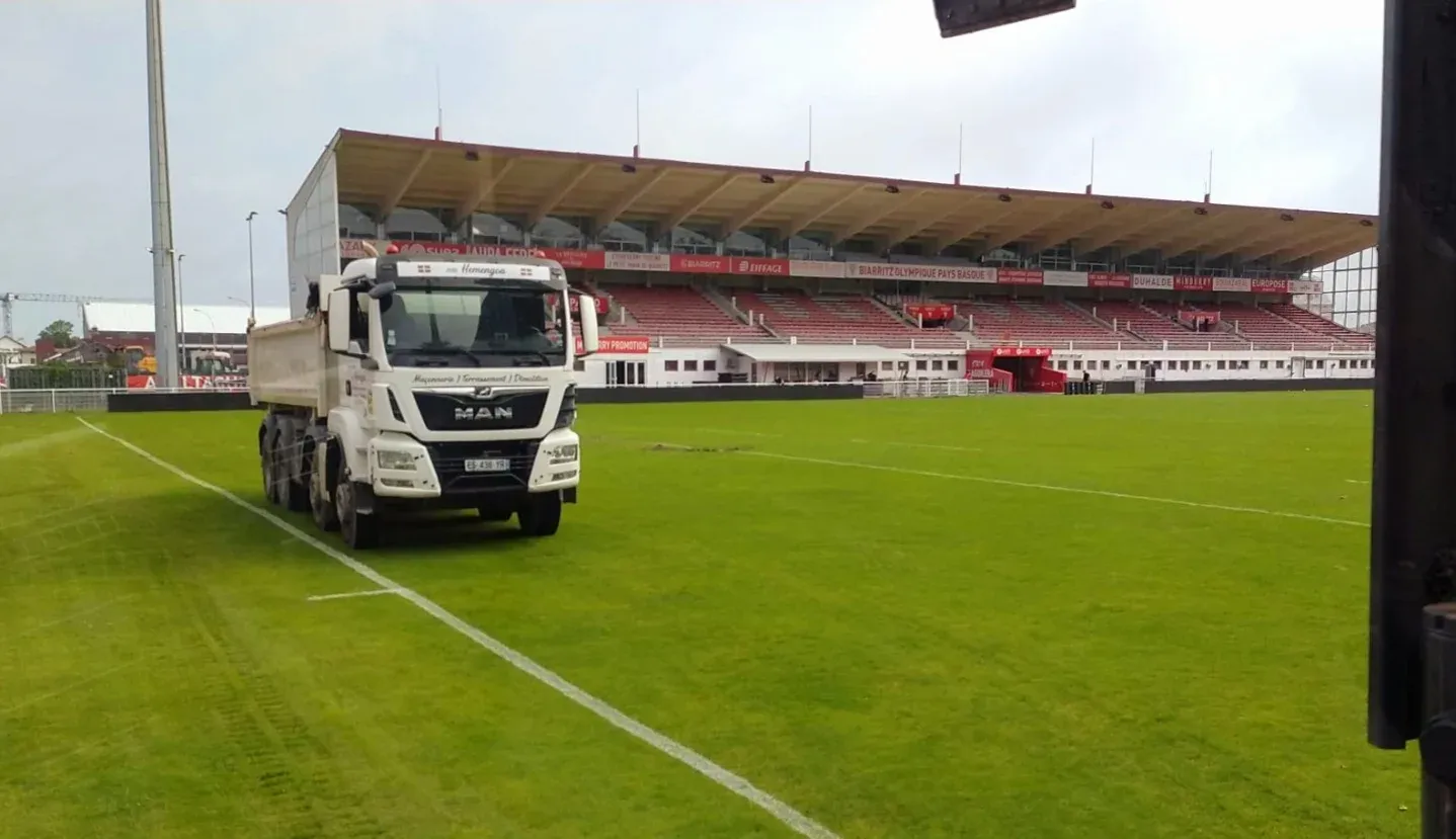 Camion benne Hemengoa sur la pelouse du Stade Aguilera, tribune en fond